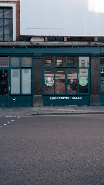 The image shows the ground floor of a commercial building with a dark teal painted facade and large windows divided into smaller panes. The entrance features a glass door with a dark frame, positioned