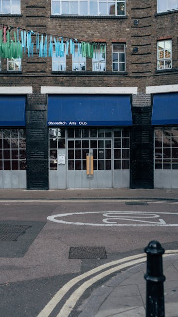 The image shows the ground floor of a commercial building with a dark teal painted facade and large windows divided into smaller panes. The entrance features a glass door with a dark frame, positioned