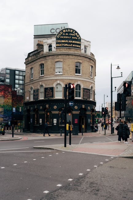 A street corner with a small café named 'Pause' occupying a brick building, featuring a wooden sign above the entrance and large glass windows revealing a cozy interior with warm lighting, hanging pe